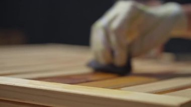 Eldivenli el ahşap bir bahçe tezgahına ahşap yağ sürüyor, yağlı ve işlenmemiş bölgeler arasında gözle görülür bir kontrast var.