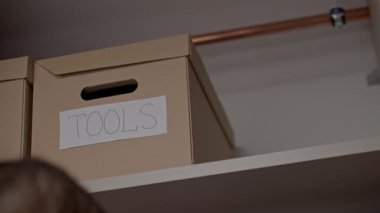 Kadın, dolapların rafına üzerinde araç gereç ve bisiklet etiketi olan karton kutular yerleştirir.