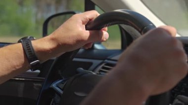 Açık alanda bulanık bir arka plan ile direksiyon simidini tutan bir erkek elini kapat.