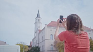Kadın, şehirdeki tarihi binaları fotoğraflamak için akıllı telefon kaldırıyor.