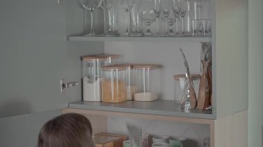 Kadın mutfak malzemelerini konteynırları rafa koyarak organize ediyor.