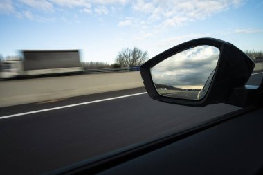 Bir spor arabadaki sol ayna manzaralı otoyolda bulutlu bir gökyüzünde