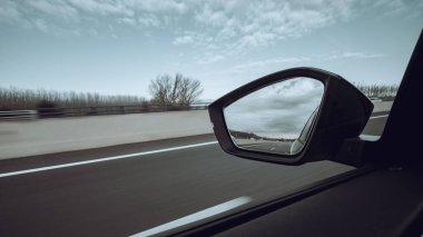 Bir spor arabadaki sol ayna manzaralı otoyolda bulutlu bir gökyüzünde