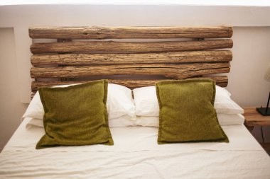 Beyaz çarşaflarda yeşil yastıklar, ahşap mobilyalar, modern iç tasarım.