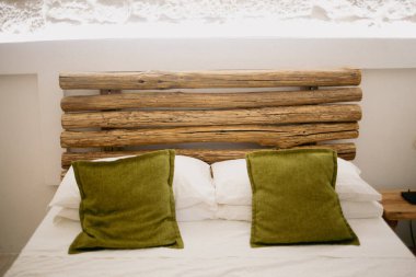 Beyaz çarşaflarda yeşil yastıklar, ahşap mobilyalar, modern iç tasarım.