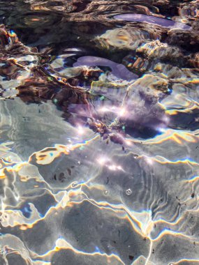 Beyaz bir kumsalda berrak şeffaf suların üzerinde parlayan ışık.