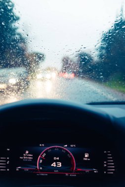Yağmurlu bir sahnede dar bir pistte, ön camında yağmur damlaları olan bir araba sürmek.