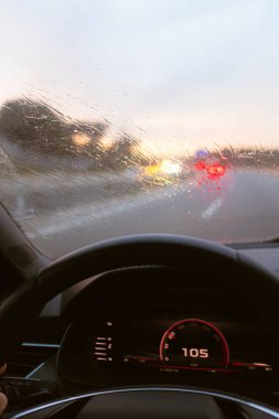Yağmur damlalarıyla dolu bir arabanın ön camı. Alacakaranlık şoförünün bakış açısından yağmurlu bir yolda araba kullanırken.