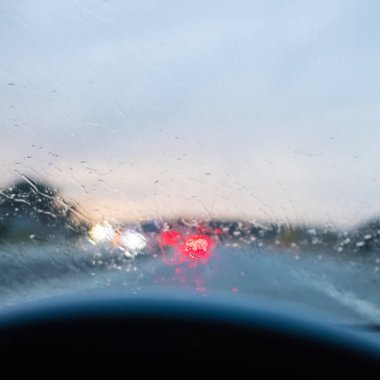 Yağmur damlalarıyla dolu bir arabanın ön camı. Alacakaranlık şoförünün bakış açısından yağmurlu bir yolda araba kullanırken.