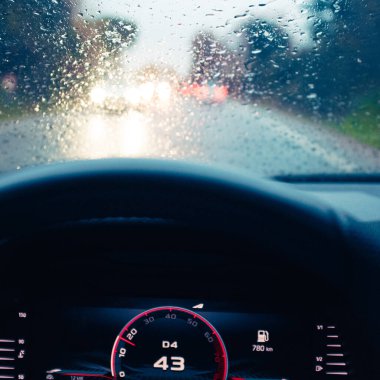 Yağmur damlalarıyla dolu bir arabanın ön camı. Alacakaranlık şoförünün bakış açısından yağmurlu bir yolda araba kullanırken.