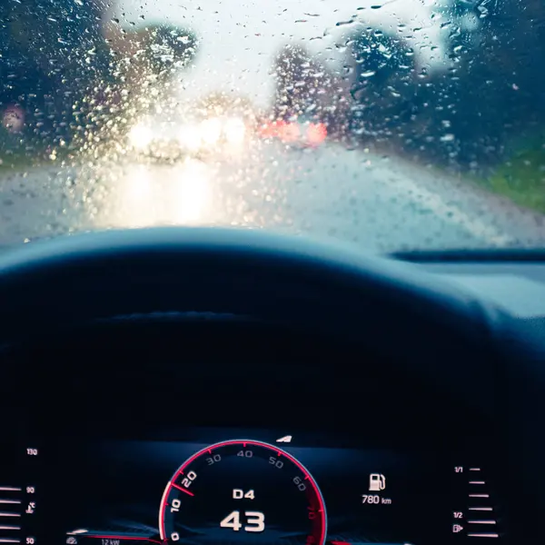 Yağmur damlalarıyla dolu bir arabanın ön camı. Alacakaranlık şoförünün bakış açısından yağmurlu bir yolda araba kullanırken.