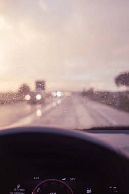 Alacakaranlıkta, yağmurlu bir yağmurun altında araba sürmek ve yol şoförünün bakış açısına göre camında yağmur damlaları olması.