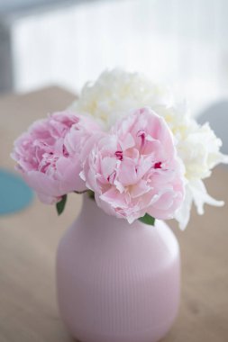 Tahta bir masada, pembe bir tencerede çiçek açan pembe şakayık çiçekleri.