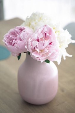 Tahta bir masada, pembe bir tencerede çiçek açan pembe şakayık çiçekleri.