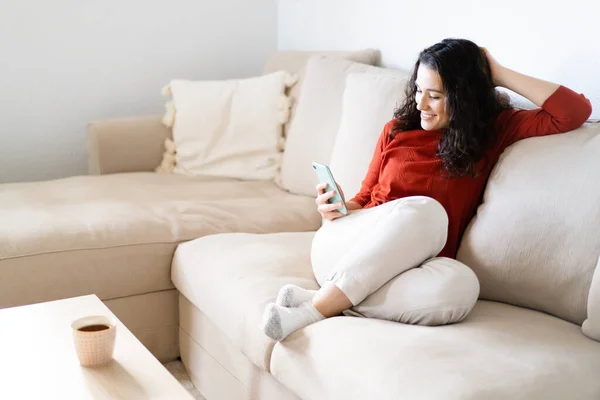 Jovem Mulher Feliz Sentada Confortavelmente Sofá Usando Seu Telefone Inteligente — Fotografia de Stock