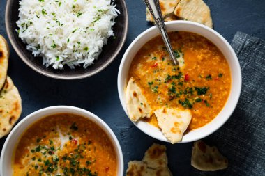 Red lentil soup with coconut milk and curry accompanied by basmati rice and naan bread on a dark blue background