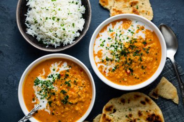Red lentil soup with coconut milk and curry accompanied by basmati rice and naan bread on a dark blue background