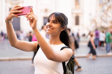 Roma 'da tatilde kalabalık bir meydanda sırt çantalı mutlu bir genç kız selfie çekiyor.