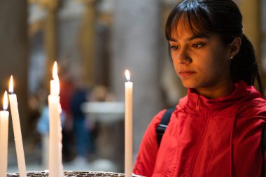 Kırmızı ceketli genç kız mum ışığında dua ediyor.