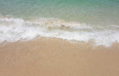 Kumlu bir plajda dalganın bir fotoğrafı var. Sahile doğru gelen bir dalga var.