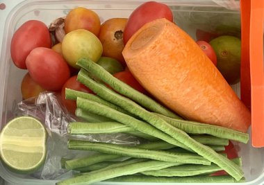 Bir konteynır dolusu limonlu sebze ve sebzenin fotoğrafı. Plastik bir kabın içinde birçok farklı meyve ve sebze var.