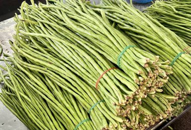 Masadaki bir grup yeşil fasulyenin fotoğrafı. Masada mavi kovalı bir sürü yeşil fasulye var.