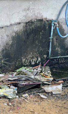 Duvarın yanındaki çöp yığınının fotoğrafı. Yerde bir yığın çöp ve bir hortum var.