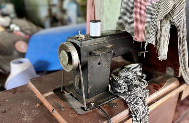 Ahşap bir masanın üstünde oturan bir dikiş makinesinin fotoğrafı. Üzerinde bez olan bir dikiş makinesi var.