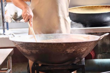 Mutfakta bir tavada yemek pişiren birinin fotoğrafı. Biri büyük bir tencereyle mutfakta büyük bir tava pişiriyor..