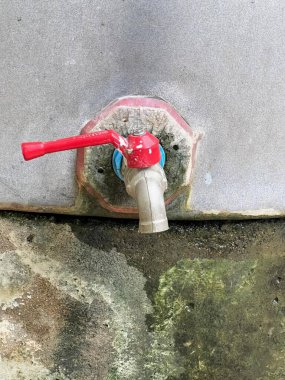 Çimento duvarında kırmızı ve mavi bir musluğun fotoğrafı var. Duvara bağlı kırmızı ve mavi bir musluk var..