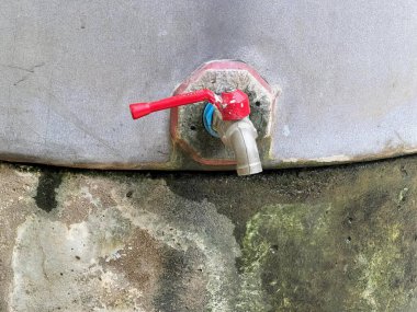 Kırmızı saplı kırmızı bir musluğun fotoğrafı. Metal bir musluğa bağlı kırmızı bir musluk var..