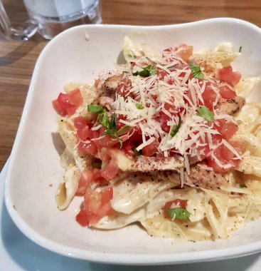 Bir tabak domates ve peynirli makarnanın fotoğrafı. Üzerinde makarna ve domates olan beyaz bir tabak var..