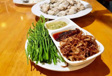 Tabaklar dolusu yemek ve bir kase sos içeren bir masanın fotoğrafı. Masada çatallı üç tabak yemek var..