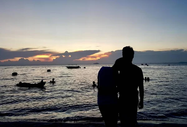 stock image a photography of a man and a woman standing on a beach, there are people standing on the beach watching the sun set.