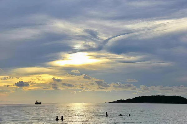 海で泳いでいる人たちの写真です ビーチには太陽が沈むのを眺めている人がいます — ストック写真