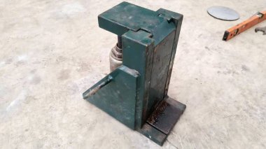 Beton zeminde duran yeşil metal bir alet tutacağının fotoğrafı. Yerde duran yeşil bir metal cihaz var..