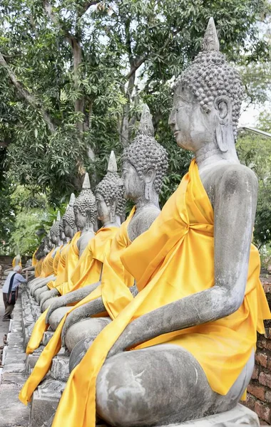 a photography of a row of buddha statues sitting on a stone wall, buddha statues lined up in a row in a park.