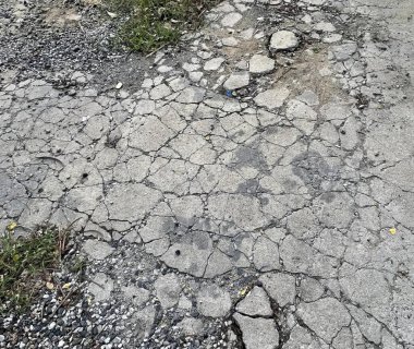 Üzerinde çatlaklar ve çimenler olan bir yolun fotoğrafı, ortasında yangın musluğu olan bir yolda rögar kapağı..