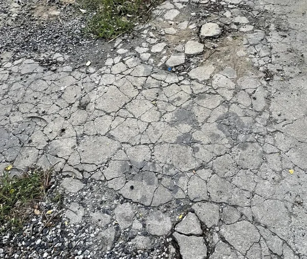 a photography of a road with cracks and grass on the side, manhole cover on a road with a fire hydrant in the middle.
