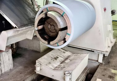 Fabrikada üzerinde büyük metal bir tüp bulunan bir kağıt, yazıcı makinesi kesen bir makinenin fotoğrafı..