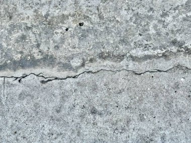Çatlakları ve çatlakları olan beton bir duvarın fotoğrafı. Ortasında çatlak olan beton bir yüzeye çivilenmiş..