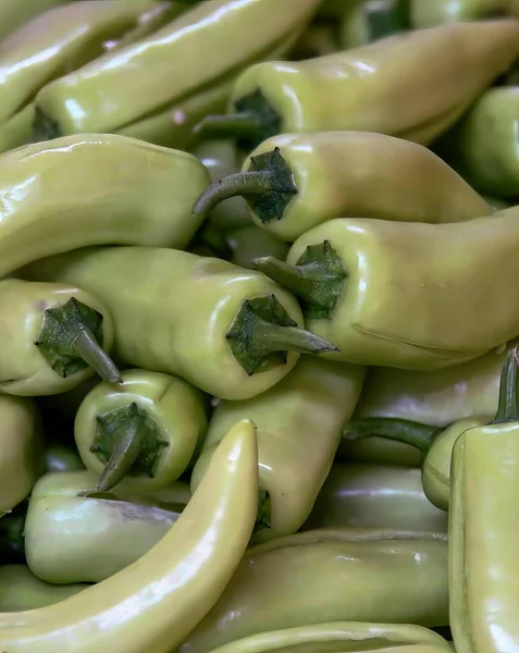 a photography of a pile of green peppers with green leaves, bell pepper peppers are piled together in a pile on a table.