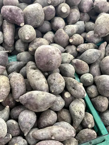 坐在桌子上的一堆土豆的照片 杂货店橱窗里陈列着绿色垃圾桶里的紫色土豆 — 图库照片