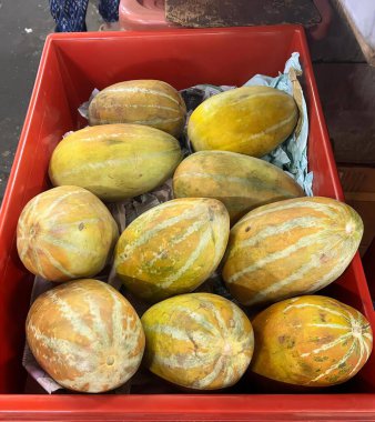 Masadaki kırmızı kutuda bir sürü olgun meyve, salatalık ve kavun dolu kırmızı bir kutunun fotoğrafı..