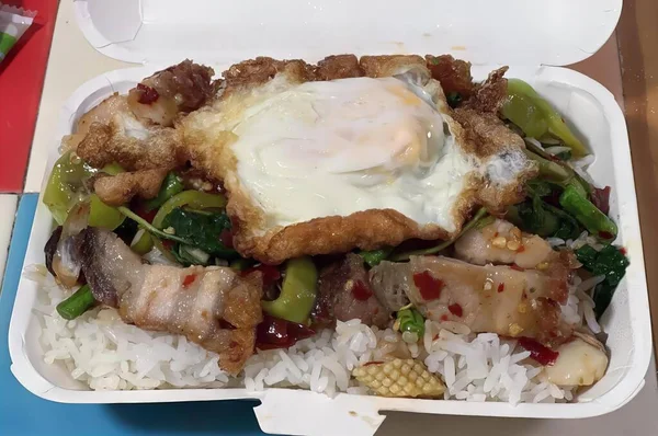 a photography of a take out box with rice, meat, and an egg, plate of food with rice, meat, and an egg in a styrofoam container.