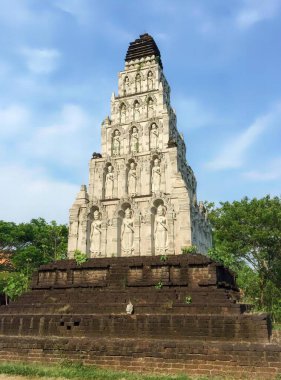 Üzerinde saat olan uzun beyaz bir binanın fotoğrafı, yeşil bir tarlanın ortasında stupa khon tapınağı..