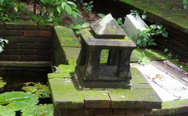a photography of a stone lantern sitting on a stone ledge, balustraded stone lantern on a stone ledge next to a pond.