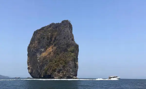 a photography of a boat passing a rock formation in the ocean, promontory of a boat passing a rock formation in the ocean.