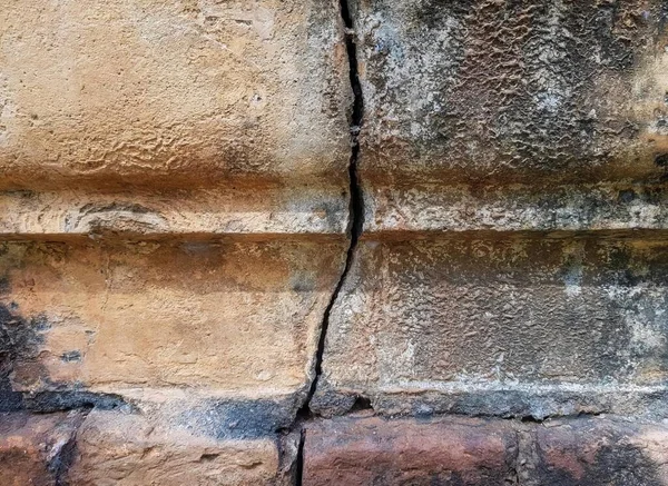 a photography of a crack in a wall with a brick wall, chain link on a brick wall with a crack in the middle.