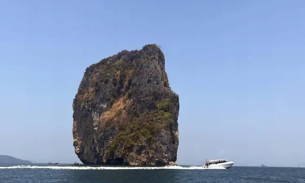 a photography of a boat traveling past a rock formation in the ocean, promontory of a boat in the water near a rock formation.